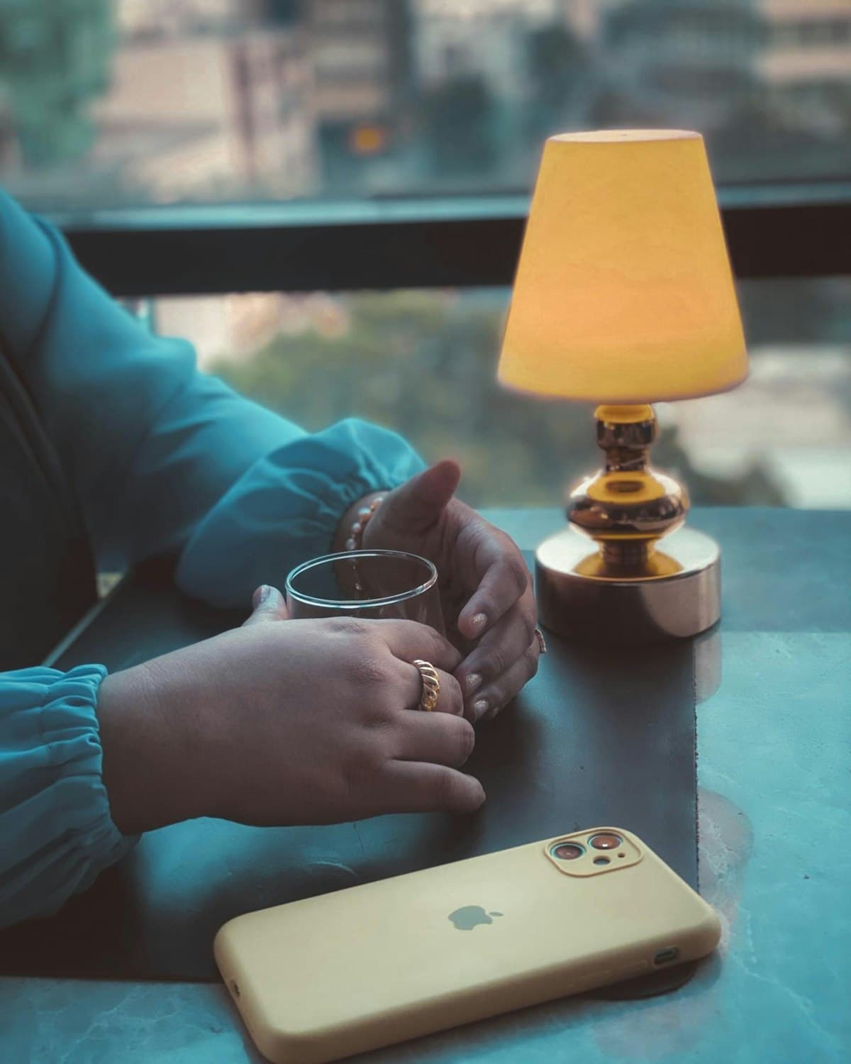 Hands cradling a cup of tea beside a warm lamp, a phone resting on the table