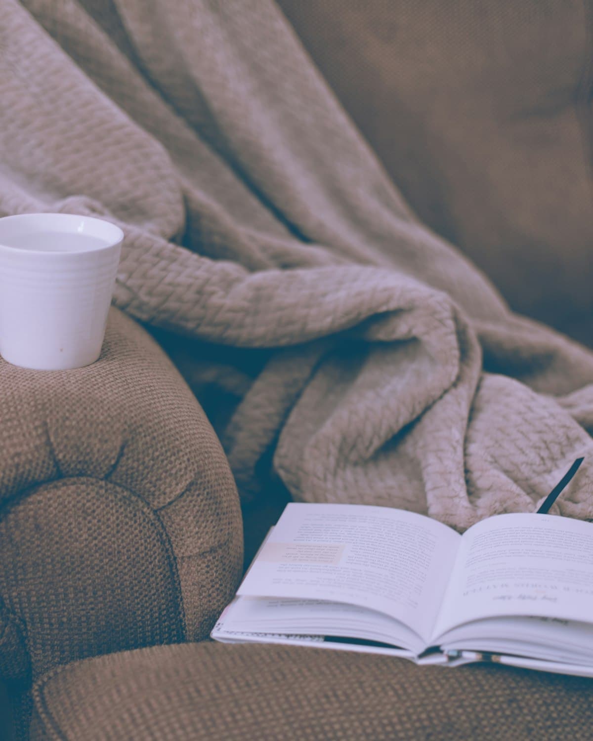 A cosy armchair with a knit blanket, a mug and an open book